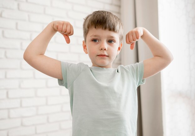 Porträt des entzückenden Jungen, der seine Muskeln zeigt