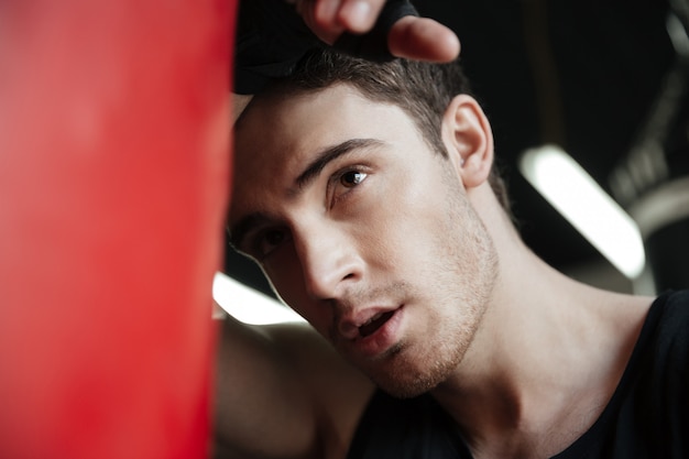 Kostenloses Foto porträt des fokussierten jungen boxers, der weg in der nähe des boxsacks schaut