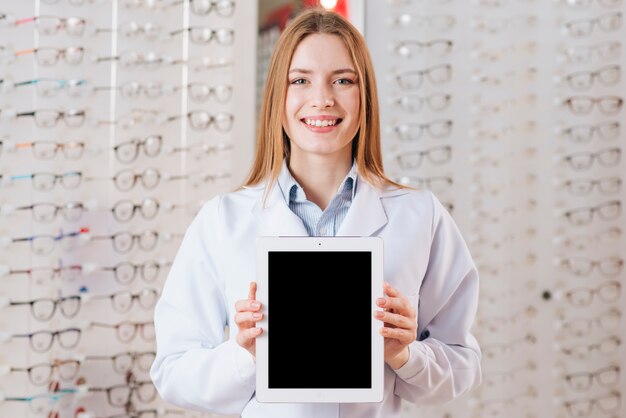 Porträt des freundlichen weiblichen Optometrikers, der Tablettenschablone zeigt