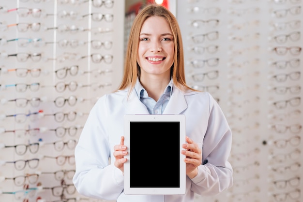 Porträt des freundlichen weiblichen Optometrikers, der Tablettenschablone zeigt