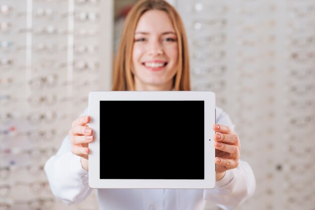 Porträt des freundlichen weiblichen Optometrikers, der Tablettenschablone zeigt