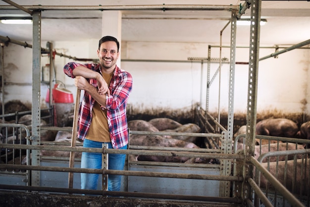 Porträt des fröhlichen Bauern, der im Viehstall auf Schweinefarm steht
