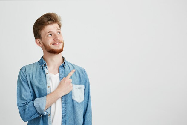 Porträt des fröhlichen jungen gutaussehenden Mannes lächelnd, der Finger oben zeigt.