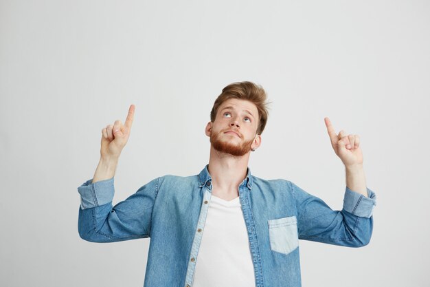 Porträt des fröhlichen jungen gutaussehenden Mannes lächelnd, der Finger oben zeigt.