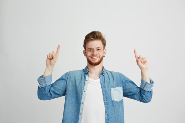 Porträt des fröhlichen jungen Mannes lächelnd, der Finger oben zeigt.