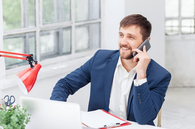 Porträt des Geschäftsmannes, der auf Handy im Büro spricht