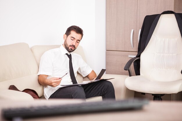 Porträt des Geschäftsmannes, der im Büro auf der Couch arbeitet, die lange Arbeitszeiten setzt. Kaufmann im beruflichen Umfeld
