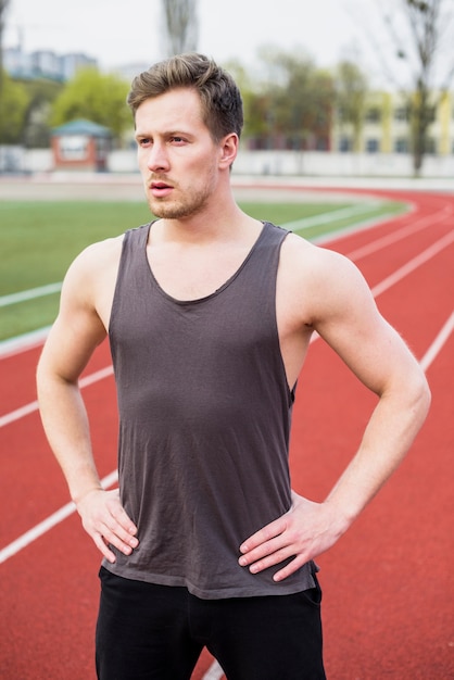 Porträt des gesunden jungen Mannes mit der Hand auf ihrer Hüfte, die auf Leichtathletik steht