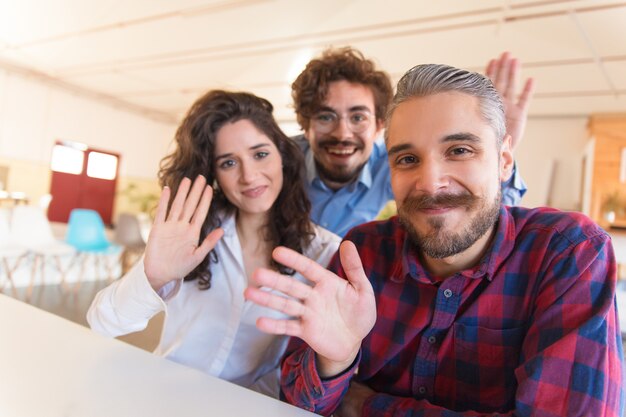 Porträt des glücklichen erfolgreichen kreativen Teams, das hallo wellenartig bewegt