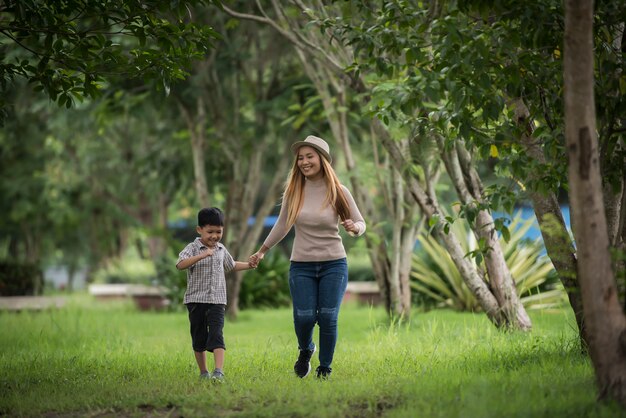 Porträt des glücklichen Gehens der Mutter und des Sohns zusammen im Park, der Hand hält.