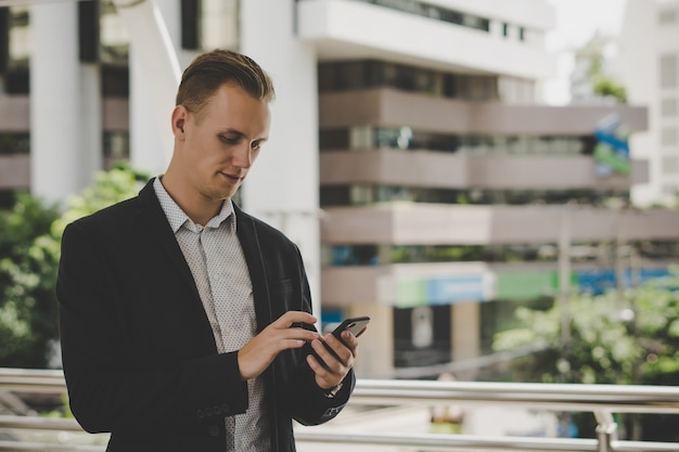 Porträt des glücklichen Geschäftsmannes, der draußen Telefon verwendet