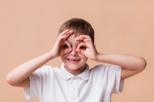 Porträt des glücklichen Jungen schauend durch Finger als Ferngläser