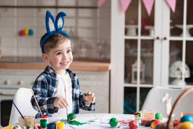 Porträt des glücklichen kleinen Jungen, der Ostereier malt