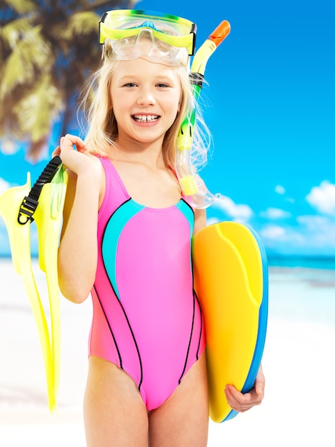 Porträt des glücklichen Mädchens, das am Strand genießt. Schulkind Mädchen steht in der hellen Farbe Badebekleidung mit Schwimmmaske auf dem Kopf.