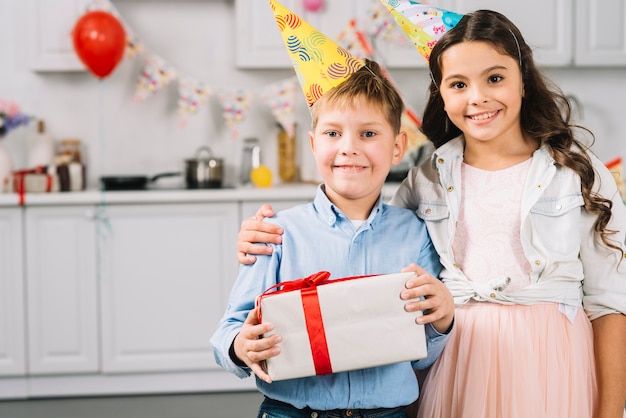 Porträt des glücklichen Mädchens mit dem Jungen, der Geburtstagsgeschenk hält