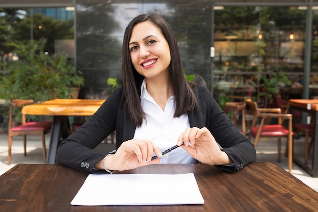 Porträt des glücklichen Managers sitzend mit Stift und Papier am Café