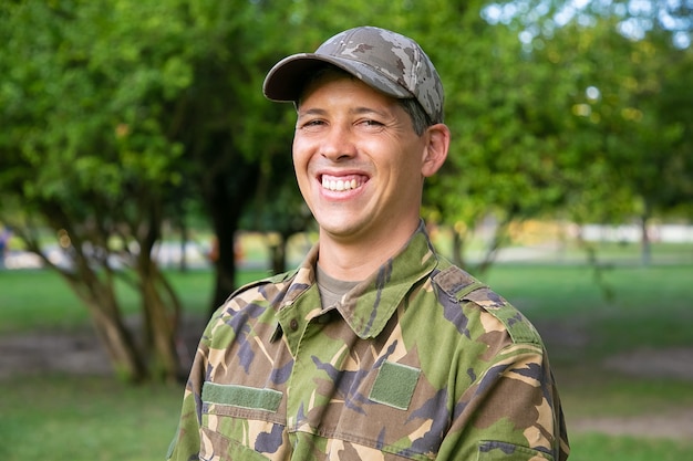 Porträt des glücklichen Mannes in der militärischen Tarnuniform, die im Park steht.