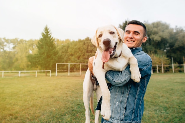 Porträt des glücklichen Mannes seinen Freund Hund Labrador bei Sonnenuntergang im Park halten