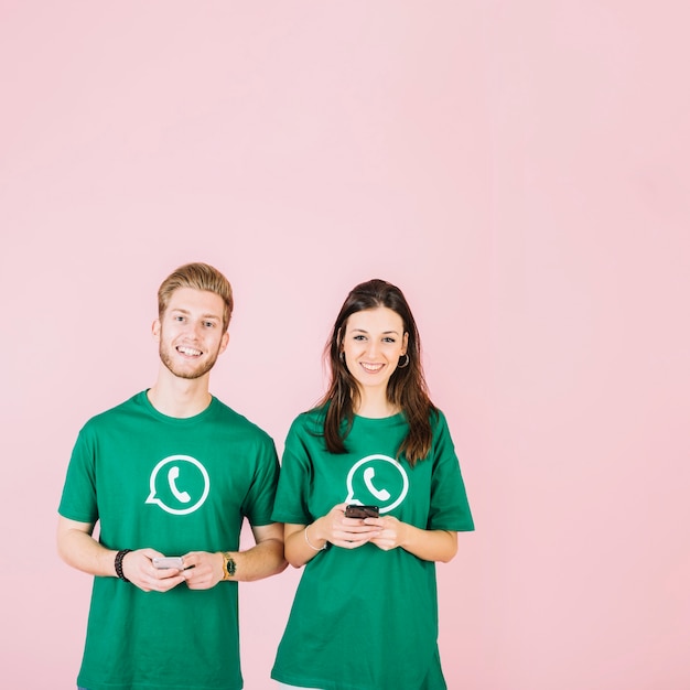 Kostenloses Foto porträt des glücklichen paars im grünen whatsapp t-shirt, das smartphone hält