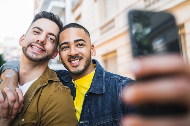 Porträt des glücklichen schwulen Paares, das Zeit zusammen verbringt und ein Selfie mit Handy in der Straße macht.