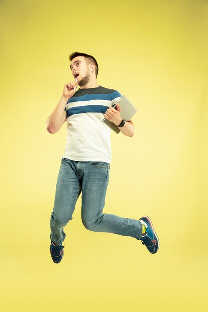 Porträt des glücklichen springenden Mannes in voller Länge mit Gadgets auf Gelb