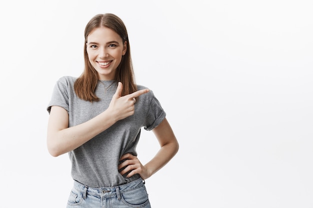 Porträt des gutaussehenden jungen kaukasischen studentenmädchens mit dunklem haar im lässigen grauen t-shirt und in den lächelnden jeans, die zähne zeigen, mit selbstbewusstem und glücklichem gesichtsausdruck,