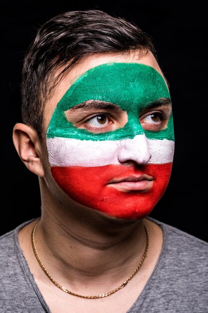 Porträt des gutaussehenden Manngesichtsanhängerfans der iranischen Nationalmannschaft mit gemaltem Flaggengesicht lokalisiert auf schwarzem Hintergrund. Fans Emotionen.