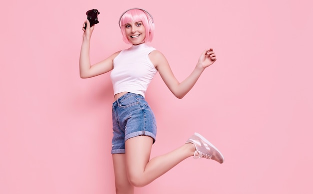 Porträt des herrlichen glücklichen Spielermädchens mit rosa Haaren, die Videospiele mit Joystick auf bunt im Studio spielen
