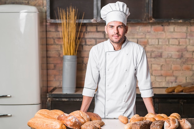 Kostenloses Foto porträt des hübschen bäckers an der bäckerei mit broten in der bäckerei