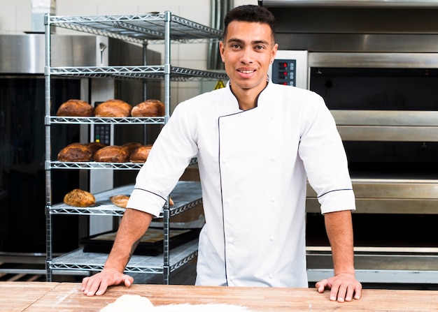 Kostenloses Foto porträt des hübschen bäckers an der bäckerei mit broten und ofen auf dem hintergrund