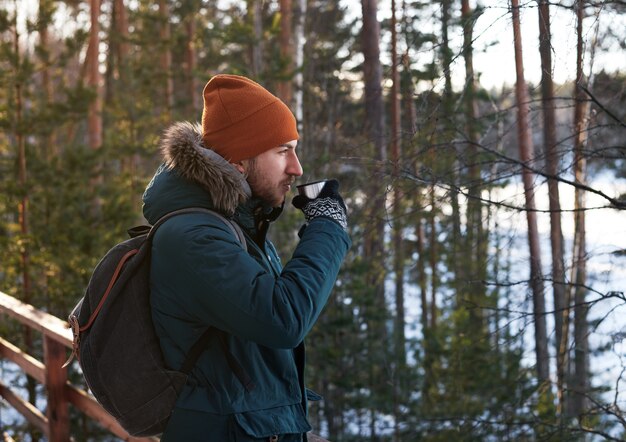 Porträt des hübschen bärtigen Mannes, der heißen Tee draußen im Waldausflug zu Fuß trinkt