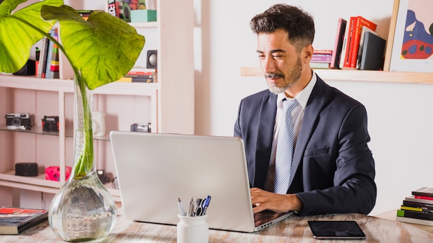 Porträt des hübschen Geschäftsmannes unter Verwendung des Laptops an seinem Arbeitsplatz