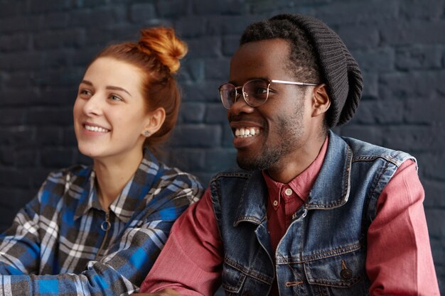 Porträt des hübschen jungen afroamerikanischen Mannes in der Brille und im Hipsterhut, die mit seiner Freundin im Café entspannen