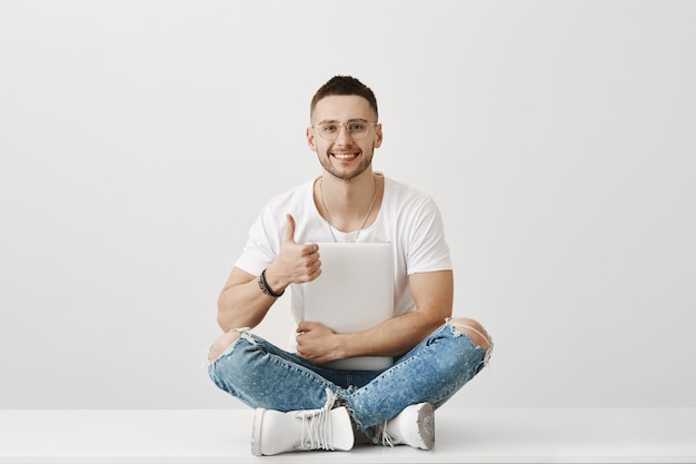 Porträt des hübschen jungen Kerls mit Brille, die mit seinem Laptop aufwirft