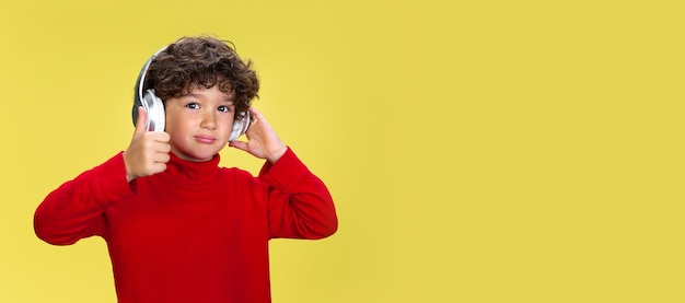 Porträt des hübschen jungen lockigen Jungen in der roten Abnutzung auf gelbem Studiohintergrund. Kindheit, Ausdruck, Bildung, Spaßkonzept.