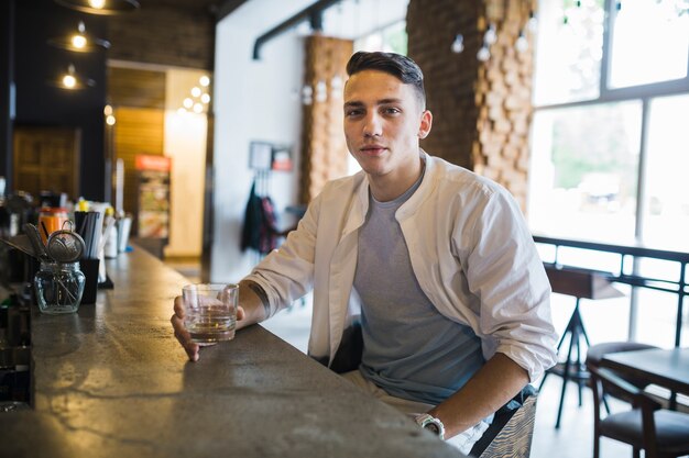 Porträt des hübschen jungen Mannes, der am Barzähler im Restaurant sitzt