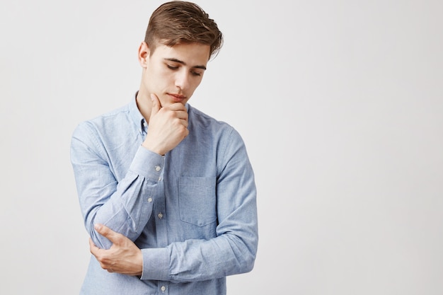 Porträt des hübschen jungen Mannes mit Hand am Kinn, nachdenklicher Blick