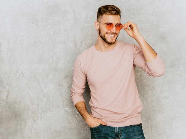 Porträt des hübschen lächelnden Modells des jungen Mannes, das zufällige Sommerrosakleidung trägt. Stilvoller Mann der Mode, der in der runden Sonnenbrille aufwirft