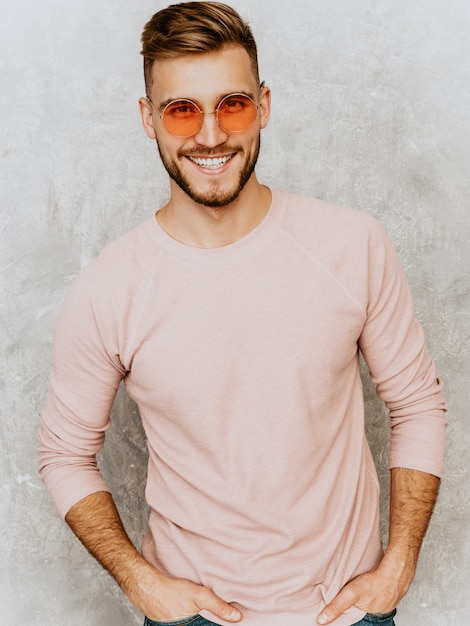 Porträt des hübschen lächelnden Modells des jungen Mannes, das zufällige Sommerrosakleidung trägt. Stilvoller Mann der Mode, der in der runden Sonnenbrille aufwirft
