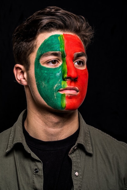 Porträt des hübschen Manngesicht-Unterstützerfans der portugiesischen Nationalmannschaft mit gemaltem Flaggengesicht lokalisiert auf schwarzem Hintergrund. Fans Emotionen.