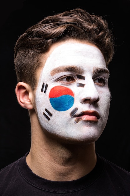 Porträt des hübschen Manngesichtsanhängerfans der Nationalmannschaft der Republik Korea mit gemaltem Flaggengesicht lokalisiert auf schwarzem Hintergrund. Fans Emotionen.