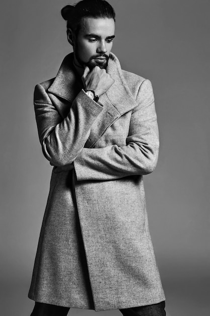 Porträt des hübschen Mode-stilvollen Hipster-Modells gekleidet im warmen Mantel, der im Studio aufwirft.