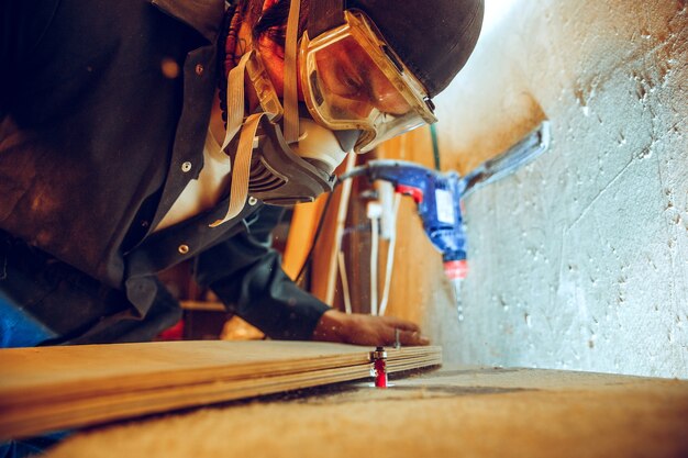 Porträt des hübschen Zimmermanns, der mit Holzschlittschuh an Werkstatt arbeitet