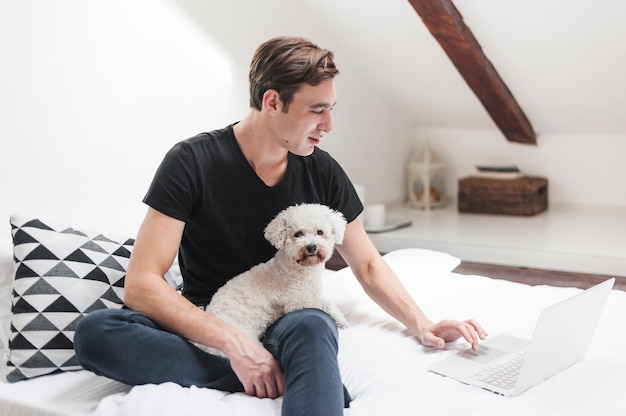 Porträt des Inhabers mit seinem freundlichen Hund, der zu Hause Laptop verwendet
