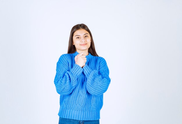 Porträt des Jugendlichmädchens in der blauen Strickjacke, die auf Weiß steht.