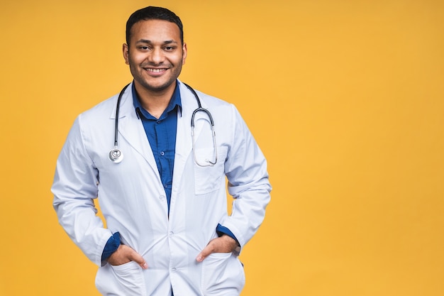 Porträt des jungen afroamerikanischen indischen schwarzen arztes mit stethoskop über dem hals im medizinischen mantel, der isoliert über gelbem hintergrund steht.
