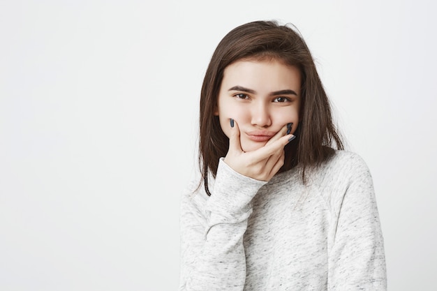Porträt des jungen düsteren Teenagers, der Unzufriedenheit ausdrückt, Mund mit Händen haltend, um Lächeln nachzuahmen
