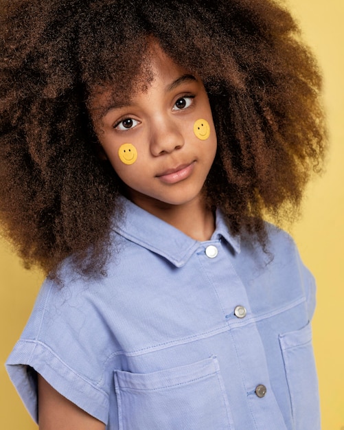 Porträt des jungen entzückenden Mädchens, das mit Emoji-Aufklebern auf ihrem Gesicht aufwirft