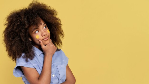 Porträt des jungen entzückenden Mädchens, das mit Emoji-Aufklebern auf ihrem Gesicht aufwirft