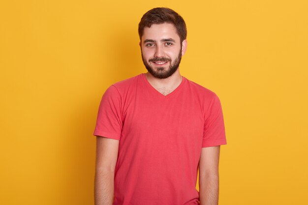 Porträt des jungen glücklichen attraktiven bärtigen Kerls, des hübschen Mannes, der rotes lässiges T-Shirt trägt, lächelnd